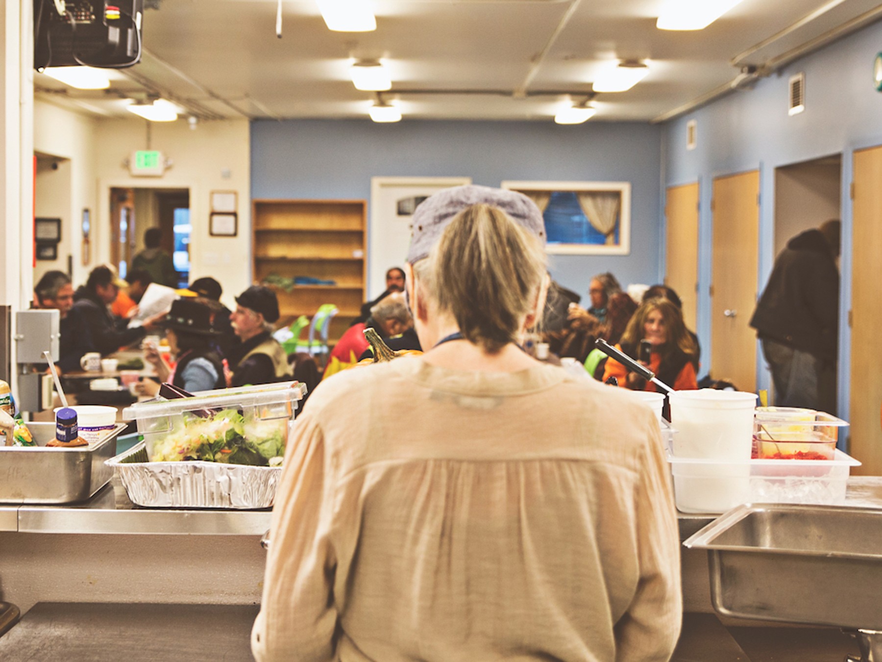 A volunteer works on preparing food at the front of a full soup kitchen.