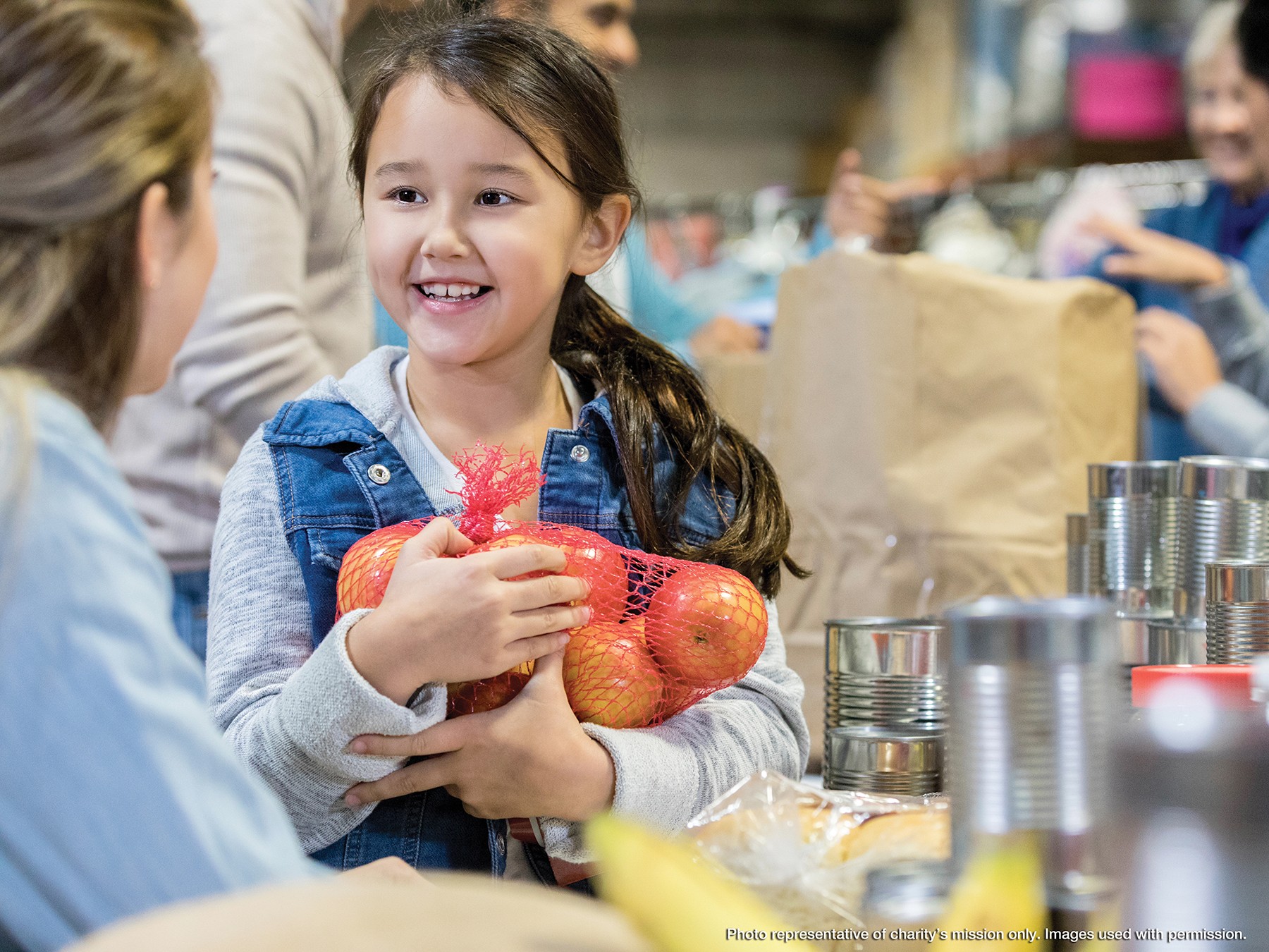 Cute elementary girl smiles as she donates a bag of apples during a community food drive.