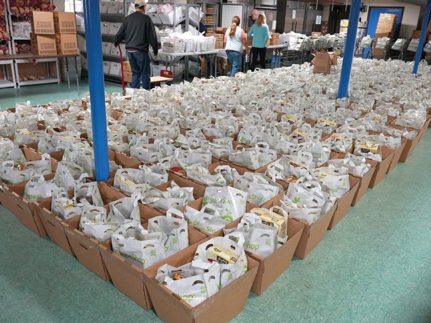 Volunteers at the food pantry organize bread, vegetables, canned goods, and eggs. They pack boxes with nutritious foods, demonstrating community teamwork. Rows of filled boxes await distribution, reflecting dedication to supporting those in need. Impact