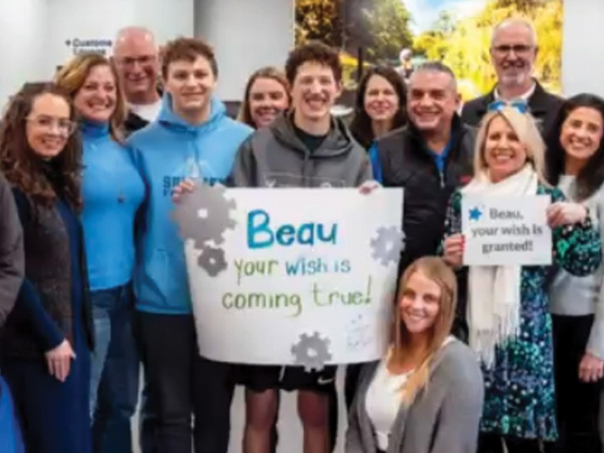 Wish kid holding sign surrounded by community members. Impact