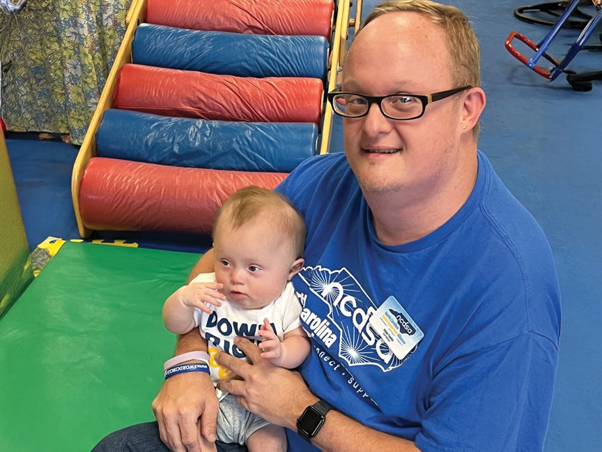 An infant with Down Syndrome interacts with an adult NCDSA Board Member and self advocate at a NCDSA playdate. Here, families and participants have enriching interactions and are able to make mentorship connections. Impact