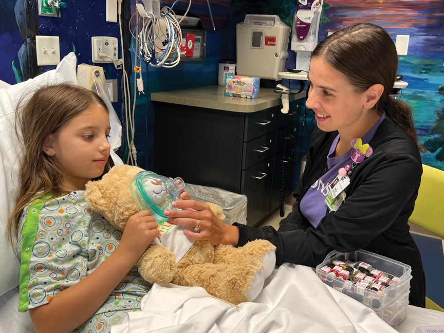 Using a stuffed animal, a child life specialist shows a pediatric patient what they can expect when getting a cast put on their arm in Bronson's Emergency Department. Impact