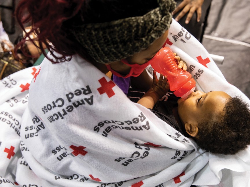American Red Cross volunteer feeding a baby with a bottle. Impact