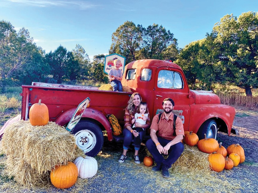 A family poses around a red truck surrounded by pumpkins during the Community Connections Family Support pumpkin patch day. Impact
