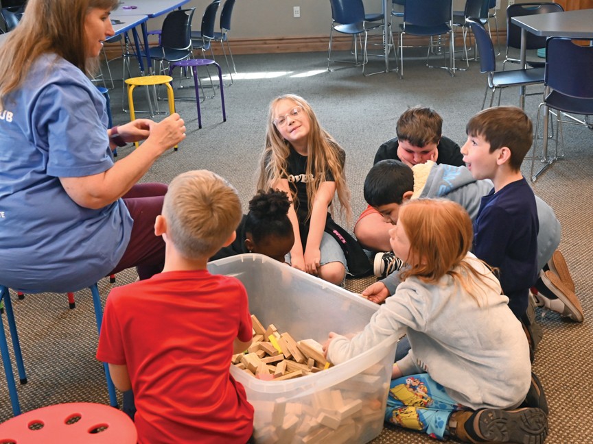 A Club staff sits in a chair and plays a game with children who are sitting on the floor. These youth received services such as meals, homework help, STEM programming, and scholarships thanks to Subaru's Share the Love Campaign. Impact