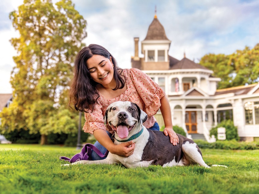 A community member and a three-legged Oregon Humane Society Salem shelter dog, who had his leg amputated at the shelter before being adopted, are sharing a happy moment on the lawn of a historic building in Salem, Oregon. Impact