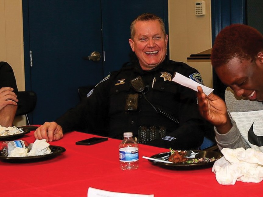 Two police officers sharing a laugh with a teen during a Feast with the Finest dinner, held after a speed dating mentorship event. Impact