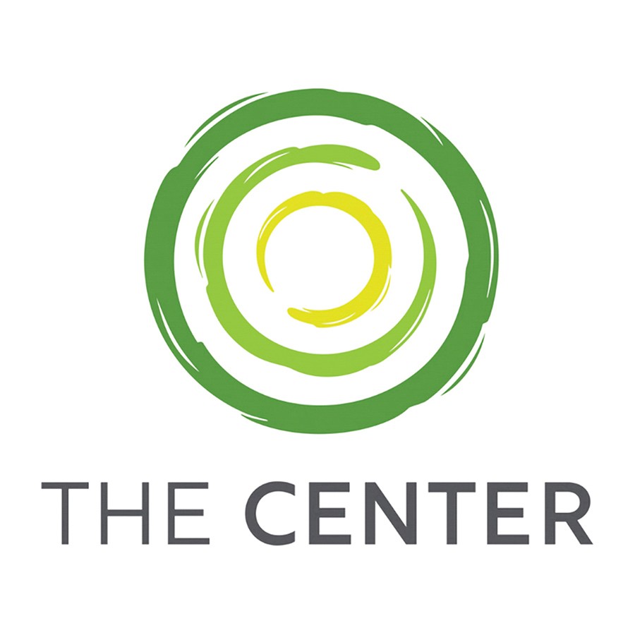 A group of smiling volunteers stands by an open car trunk filled with wrapped gifts, holding a Subaru Share the Love Event sign.