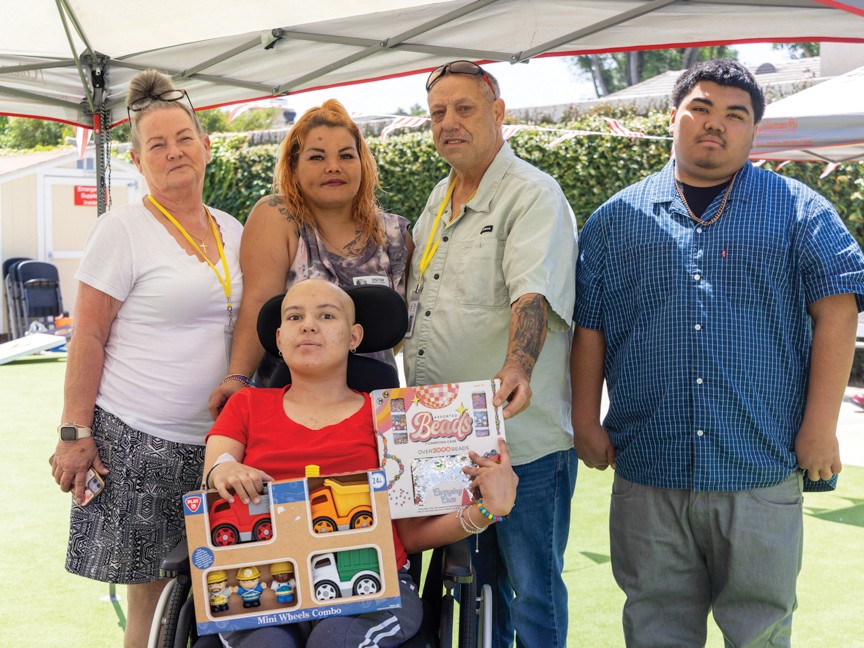 Family at the House's annual Family Summer Carnival, hosted by onsite Family Support Services. The family is showing off the prizes that their daughter, who is in the process of receiving vital medical care, won at the carnival. Impact