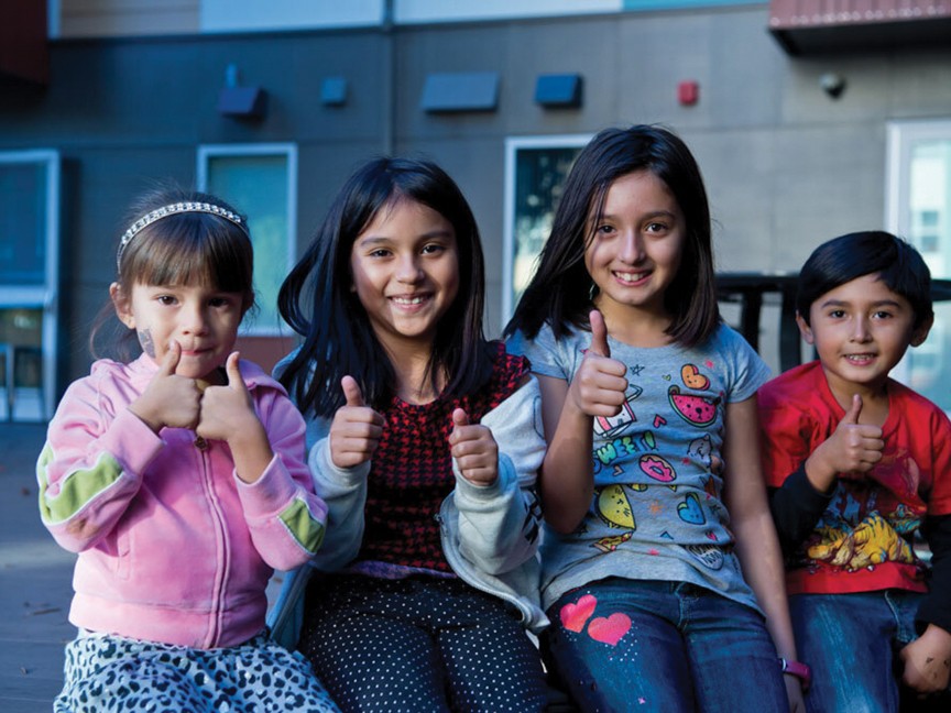 A group of children, helped through our program, smiling and showing thumbs up. Impact